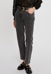 Jeans negros de cintura alta con un corte relajado, que cuentan con cinturillas y un ligero desgaste. Combinados con unos mocasines negros brillantes y una blusa negra transparente.