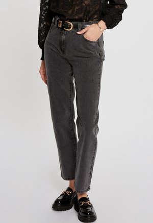 Black high-waisted jeans with a relaxed fit, featuring belt loops and subtle distressing. Paired with shiny black loafers and a sheer black top.