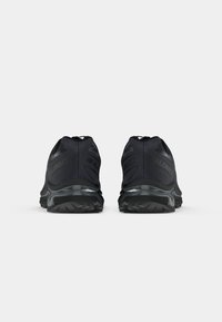 Pair of black Salomon running shoes viewed from the back, showing rugged soles and heel cushioning on a plain gray background.