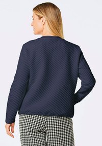 Marineblaue gesteppte Sweatshirt mit einer kastigen Form und Rundhalsausschnitt, kombiniert mit schwarz-weißen Hahnentrittmuster-Hosen.