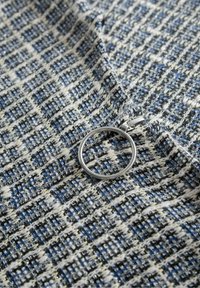 Kudottu kangas, jossa on sininen, musta ja valkoinen ruutukuosi metallilangalla. Mukana hopeinen renksulaukku.