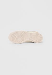 Podešev béžové tenisky Nike ukazující kruhové a mřížkové vzory běhounu s vyraženým logem Nike uprostřed.