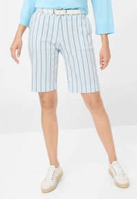 Shorts rayés bleu clair et blanc avec une texture lisse, ajustement tailleur et une ceinture blanche. Assortis à des baskets blanches à lacets.