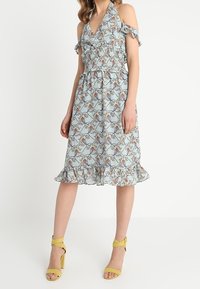 Ljusblå klänning med blommönster, volangärmar och en flerlagrig kant. Matchad med gula snörskor för accent.