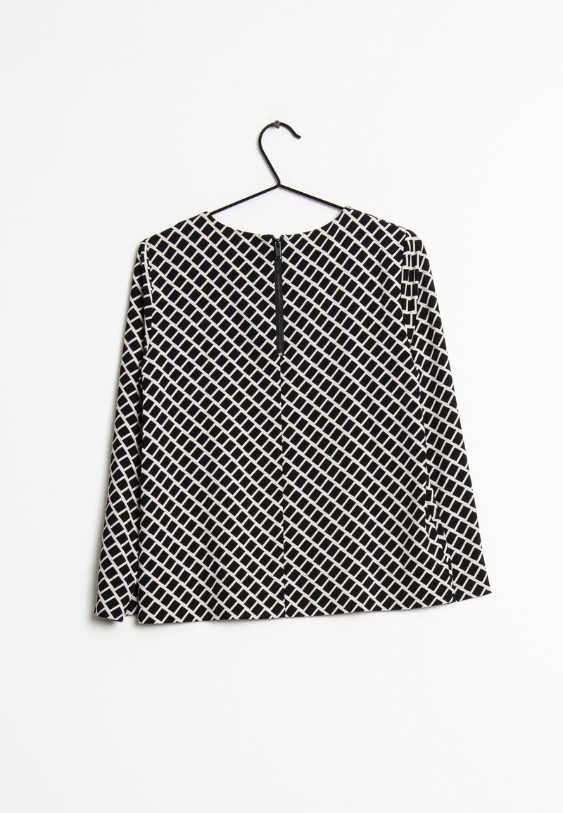 Svart och vit långärmad topp med ett diamantmönster, rund halsringning och dragkedjestängning bak, hängande på en svart krok.