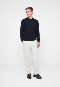 Granatowy sweter polo z dzianiny w warkocze, zestawiony z jasnoszarymi spodniami i brązowymi loafersami, charakteryzujący się klasycznym krojem i ribbowymi mankietami.