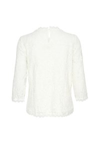Blouse en dentelle blanche à manches trois-quarts, avec un ourlet festonné et une fermeture à boutons au dos. Présente des motifs floraux complexes tout au long.