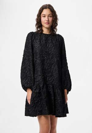 Melnā teksturētā kleita ar garām balona piedurknēm, savilkta josta un līmeņu volāni apakšmalā. Izgatavota no krunkotas auduma, bez redzamām aizdarem.