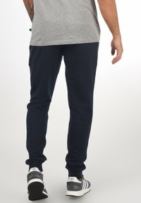 Navy joggers made from soft material with a slim fit, featuring ribbed cuffs and worn with grey and white sneakers.