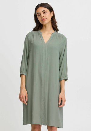 Robe longueur genou, décolleté en V en tissu vert doux avec un motif de grille subtil, dotée de manches trois-quarts et de poignets élastiques.
