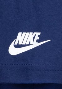 Temno modra majica s poudarjenim belim logotipom Nike in obliko požarka, izdelana iz mehke bombažne tkanine, prikazana z natančnimi detajli šivanja.