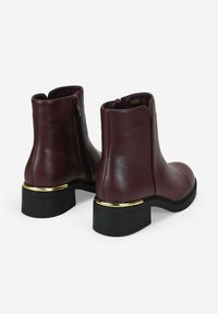 Bottes de cheville en cuir bordeaux à bout rond, avec une fermeture éclair latérale et un talon noir mis en valeur par une bande dorée.