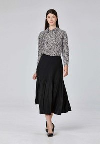 Jupe noir plissée associée à un chemisier blanc à manches longues avec un petit motif floral noir. Comprend des chaussures à talons hauts noires.