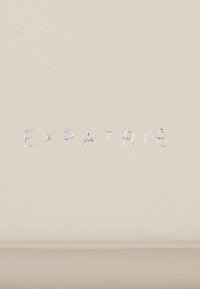 Lettres métalliques argentées épelant "EXPATRIE" sur un fond en cuir lisse beige clair.