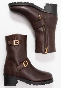 Hnědé kožené kotníkové boty s bočním zipem, nastavitelním páskem se zlatou sponou, texturovaným povrchem a vrstveným podpatkem.
