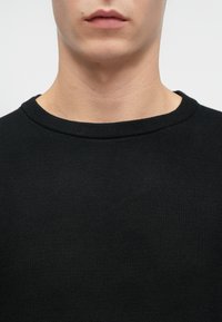 Czarny dzianinowy sweter z okrągłym dekoltem, wykonany z gładkiej, teksturowanej tkaniny. Zbliżenie na obszar kołnierza i otaczającą skórę.