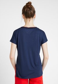 Granatowa koszulka z krótkim rękawem i okrągłym dekoltem, z paskowanym akcentem przy kołnierzu oraz zaokrąglonym dołem. Gładka tekstura materiału.