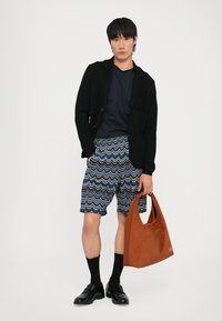 Melns teksturēts žakets, tumši zils T-krekls, rakstainas zilas šortus ar viļņotu dizainu, melnas zeķes, melnas kurpes un oranžs-brūns somu maciņš.