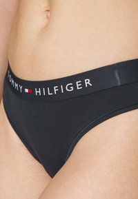 Culotte en coton noir avec une ceinture noire arborant le texte et le logo "TOMMY HILFIGER" en blanc. Texture lisse, design semi-haute taille.