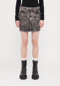 Jeansowa spódnica w wyblakłym czarnym kolorze z wzorami gwiazd, z pięcioma kieszeniami, zamkiem błyskawicznym i szlufkami na pasek, w połączeniu z czarnymi ciężkimi botkami i białymi skarpetkami.