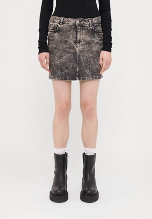 Jeansrock in verblasstem Schwarz mit Sternmustern, ausgestattet mit fünf Taschen, einem Reißverschluss und Gürtelschlaufen, kombiniert mit schwarzen klobigen Stiefeln und weißen Socken.