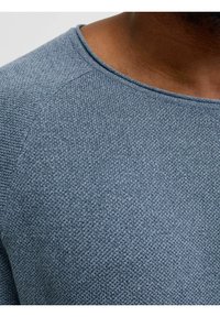 Gestrickter Pullover aus einem weichen, strukturierten blauen Stoff. Mit rundem Ausschnitt und Raglanärmeln für eine angenehme, bequeme Passform.