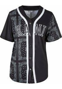 Sort kortærmet trøje med bandana-mønster, hvide detaljer og kontrastfarvede sorte knapper. Har "KANI" trykt på forsiden.