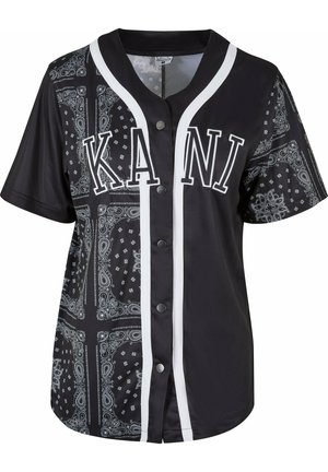 Svart kortärmad tröja med bandana-mönster, vita detaljer och kontrasterande svarta knappar. Har "KANI" tryckt på framsidan.