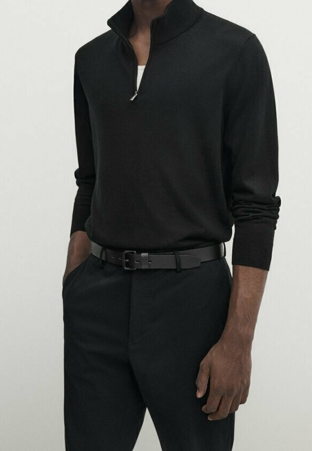 Pull noir à fermeture quart de zip en tissu lisse, associé à un pantalon noir sur mesure et une ceinture noire, présentant un design élégant et une silhouette ajustée.