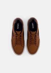 Bruna lädersneakers med en slät yta, vit gummisula och svart inredning. Har sydda detaljer och logotyp på tungan.