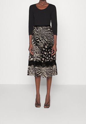 Vrouw draagt een zwart shirt met lange mouwen en een midilengte rok met verschillende dierenprintpatronen, gecombineerd met zwarte open-toe hakken.