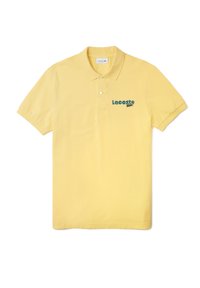 Camisa polo amarilla de algodón, con una tapeta de tres botones y el logo bordado en verde de "Lacoste" en el lado izquierdo del pecho.