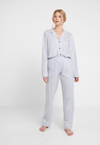 Randig pyjamaset i ljusblått och vitt, med långa ärmar, knäppning framtill och byxor med elastiskt midjeband och avslutade fållar.