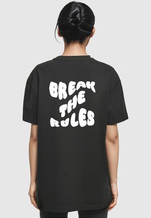 Black oversized t-shirt featuring white bubble text on the back that reads "BREAK THE RULES." Short sleeves and a crew neck design.