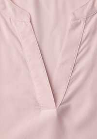 Tissu rose clair avec un décolleté en V profond présentant un détail de couture double sur les bords.