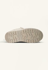 Beige sneaker sole with a textured rubber pattern, featuring a hexagonal design and brand marking. Sturdy and designed for traction.