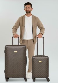 Deux valises à motifs marron de tailles variées avec des accents dorés, une texture lisse et des poignées rétractables, reposant sur des roues.