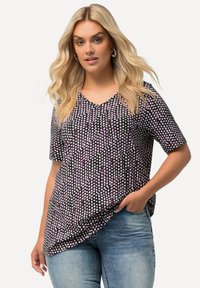Top de manga corta en tejido negro con un estampado de lunares blancos y morados, que presenta un escote en V y un dobladillo ligeramente curvado.