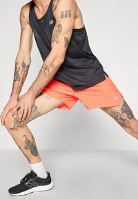 Must olema must sporditopp, erksad oranžid lühikesed püksid ja mustad jooksujalatsid. Käte ja jalgade peal on nähtavad tätoveeringud. Minimalistlik disain ja värvid.