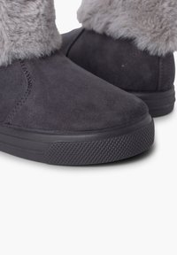 Botas de ante gris con un suave puño de piel sintética gris. Presentan una suela de goma negra texturizada para mayor agarre. Superficie lisa sin patrones visibles.