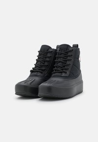 Botas de goma negras con un eje de nailon acolchado, diseño con cordones, suelas texturizadas y una lengüeta de tira en la parte trasera, con un branding minimalista.