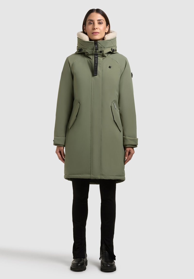 Olivovo zelený prešívaný kabát s vysokým golierom a béžovým umelým kožuchom. Obsahuje zipsové vrecká a predné zapínanie na zips.