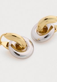Pendientes de metal dorado y plateado con un diseño circular y una sección superior curvada y brillante. La superficie es suave y reflectante.