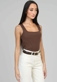 Débardeur marron à côtes avec des bretelles larges et un décolleté carré, associé à un jean blanc taille haute et une ceinture marron foncé.