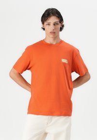 Oranje katoenen T-shirt met een ronde hals en korte mouwen, voorzien van een klein wit 'SAINT-TROPEZ' logo op de linkerkant van de borst.