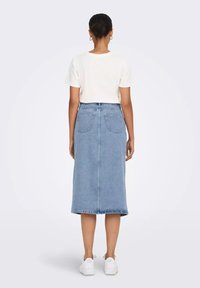 Jupe en denim bleu clair à coupe droite, avec deux poches arrières et un ourlet brut, assortie à un haut blanc à manches courtes et des baskets blanches.