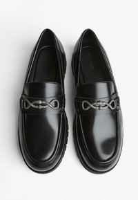 Fekete bőr loaferek fényes bevonattal, az elején textúrázott ezüst láncszerű díszítéssel és lekerekített orrkialakítással.