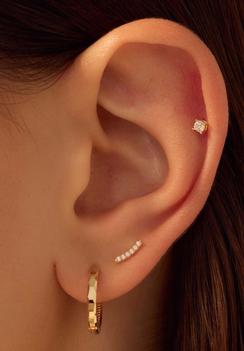 Gold hoop earring with a textured design and a small diamond stud. Also, a bar earring featuring four tiny, embedded clear stones.