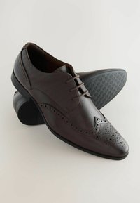 Chaussures de ville en cuir marron avec une finition lisse, un bout pointu, des perforations décoratives et une semelle en caoutchouc noir texturé.