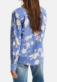 Camicia a maniche lunghe blu a motivi floreali bianchi, con orlo arrotondato e polsini con bottoni, realizzata in tessuto leggero.
